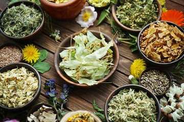 Herb selection and fresh flowers in bowls on wooden background