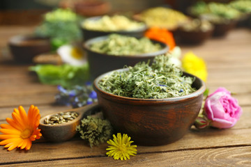 Herb selection and fresh flowers in bowls on wooden background