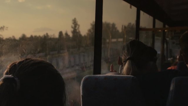 Girl travels in a bus looking out the window at sunset