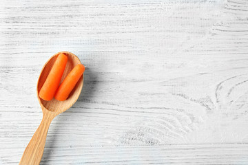 Small baby carrots in spoon on light wooden background