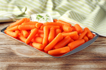 Baby carrots and saucer with cream in silver tray on wooden background