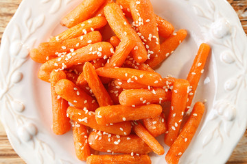 Cooked baby carrots with sesame in white plate, close up