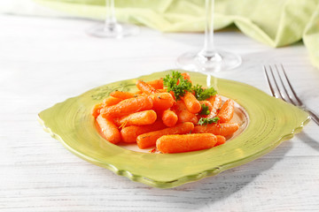 Cooked spiced baby carrots in green plate on light wooden background