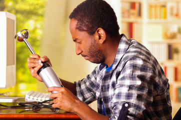 Man sitting by desk repairing handheld blender using hands, upset and annoyed facial expressions...