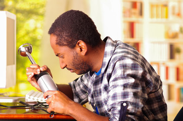 Man sitting by desk repairing handheld blender using hands, upset and annoyed facial expressions while working