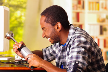 Man sitting by desk repairing handheld blender using hands, upset and annoyed facial expressions while working