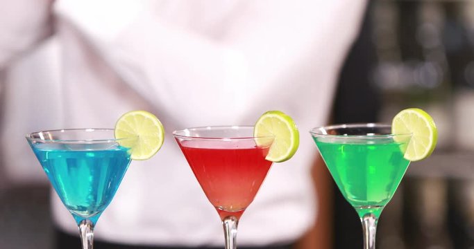 Smiling barkeeper serving colored cocktails
