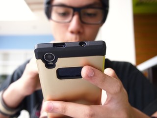 Teenager wearing a bonnet and eyeglasses using a smartphone
