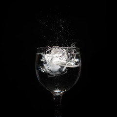 Water splash with ice in glass on black