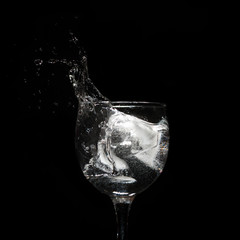Water splash with ice in glass on black