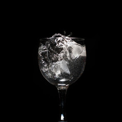 Water splash with ice in glass on black