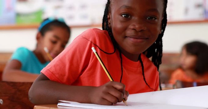 Little girl writing and smiling at camera during class in elementary school