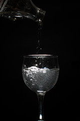 Pour water into a glass on black background.