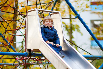 kid boy climbing on outdoor playground on autumn day