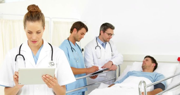 Doctors speaking with sick patient in bed while one checks tablet