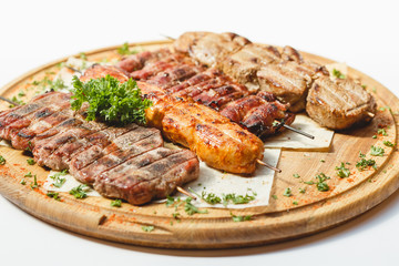 Different kind of grilled meat skewers on the wooden plate on white background