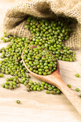 close up green mung beans in wooden spoon on wood plate