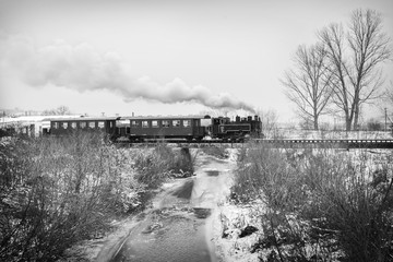 Obraz premium Vintage steam train puffing through countryside during wintertime