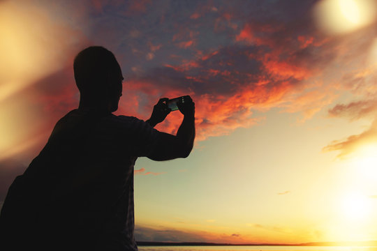 A man takes a photo of the sunset on your smartphone