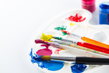 Obraz premium Colorful paints on palette and brushes on white background