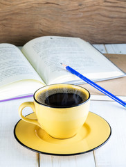 Yellow cup of Hot coffee and book, pencil on the table white wood