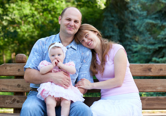 happy family portrait with baby girl on outdoor, sit on wooden bench in city park, summer season,...