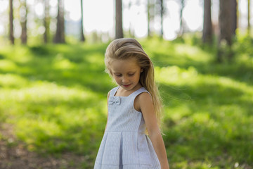 portrait of a beautiful girl with long blond hair in a light dress, walking in the woods on a sunny day