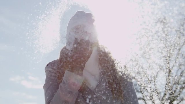 SLOW MOTION: Smiling young woman blows snowflakes in sunny winter