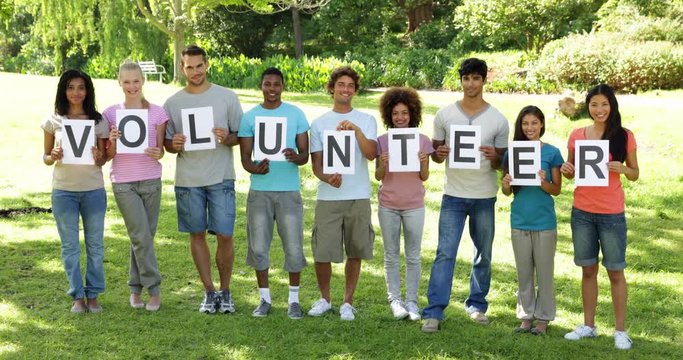 Group of casual young friends smiling at camera holding letters spelling volunteer 