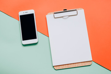Creative flat lay of smartphone and blank clipboard on minimal c