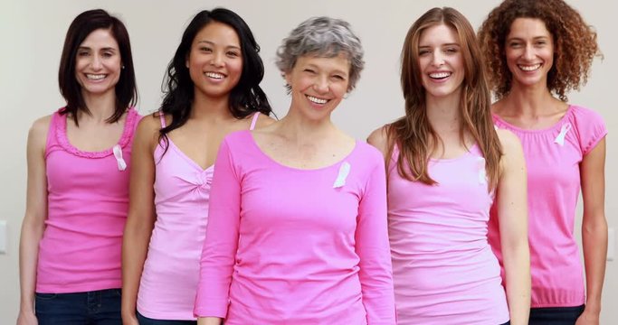 Happy women standing in a row with pink ribbon on shirt