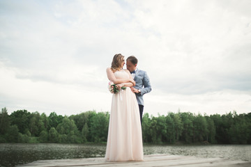 Fototapeta na wymiar Bride and groom walking on the river, smiling, kissing