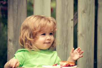 Fototapeta premium small boy eating pie near wooden fence
