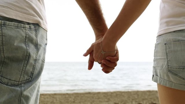 Couple holding hands on the background of the sea. Close-up of hands against the sea.  Love, romance, newlyweds. Man and woman holding hands on the beach.