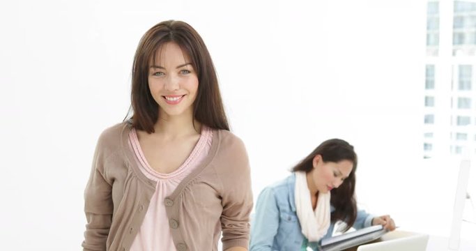 Creative businesswoman smiling at camera with colleague behind her