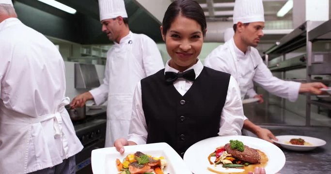 Smiling waitress showing two dishes to camera