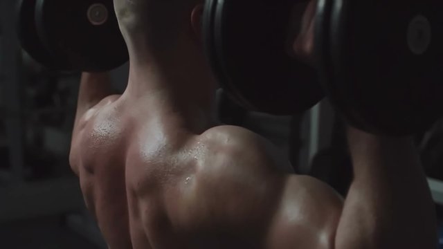 Bodybuilder lifting up heavy dumbbells in the dark gym
