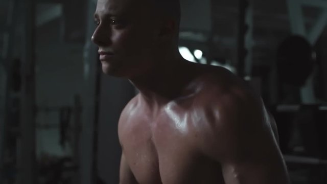 Handsome young man with naked sweating torso doing side raise with dumbbells