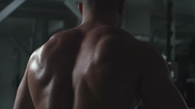 Rear view of man with naked sweating back doing side raise with dumbbells