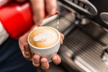 Closeup of barista pouring milk into art cappuccino