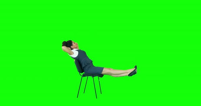 Attractive woman witting on chair with legs up and hands behind head on green screen