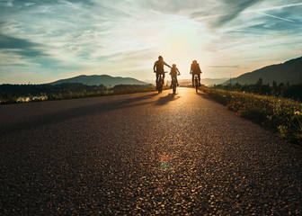 Cyclists family traveling on the road at sunset - obrazy, fototapety, plakaty