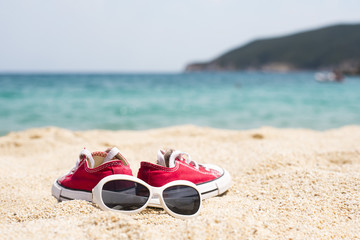 Close up of sunglasses and red sneakers on the beautiful sand beach as summertime concept