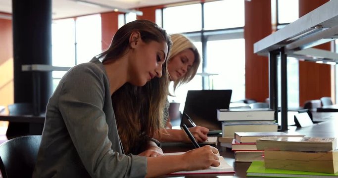 Mature student with classmates writing notes at desk in library