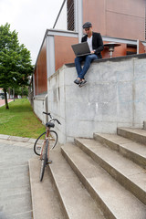Young man with Irish beret sitting on a wall with a ladder and his bicycle near