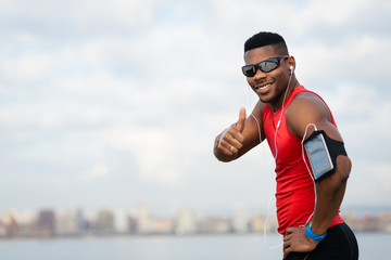Positive urban black athlete celebrating running workout success towards city skyline background....