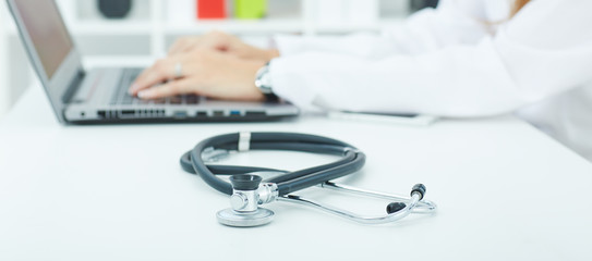 Medical stethoscope lying on the desk closeup while medicine doctor working in background. Health,...