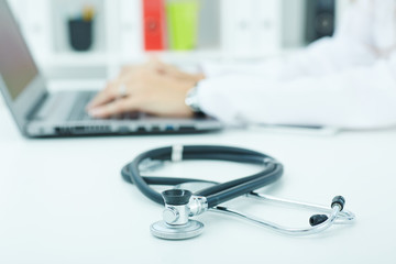 Medical stethoscope lying on the desk closeup while medicine doctor working in background.Health,...