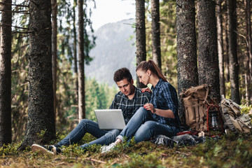 A couple of tourists sitting and looking at laptop in the woods. The concept of active rest