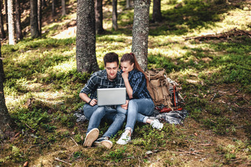 Fototapeta premium A couple of tourists sitting and looking at laptop in the woods. The concept of active rest